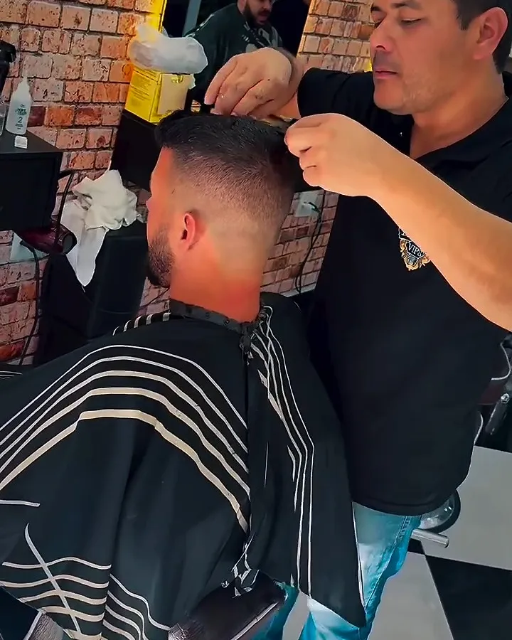Barbeiro finalizando o corte degradê de um cliente adulto