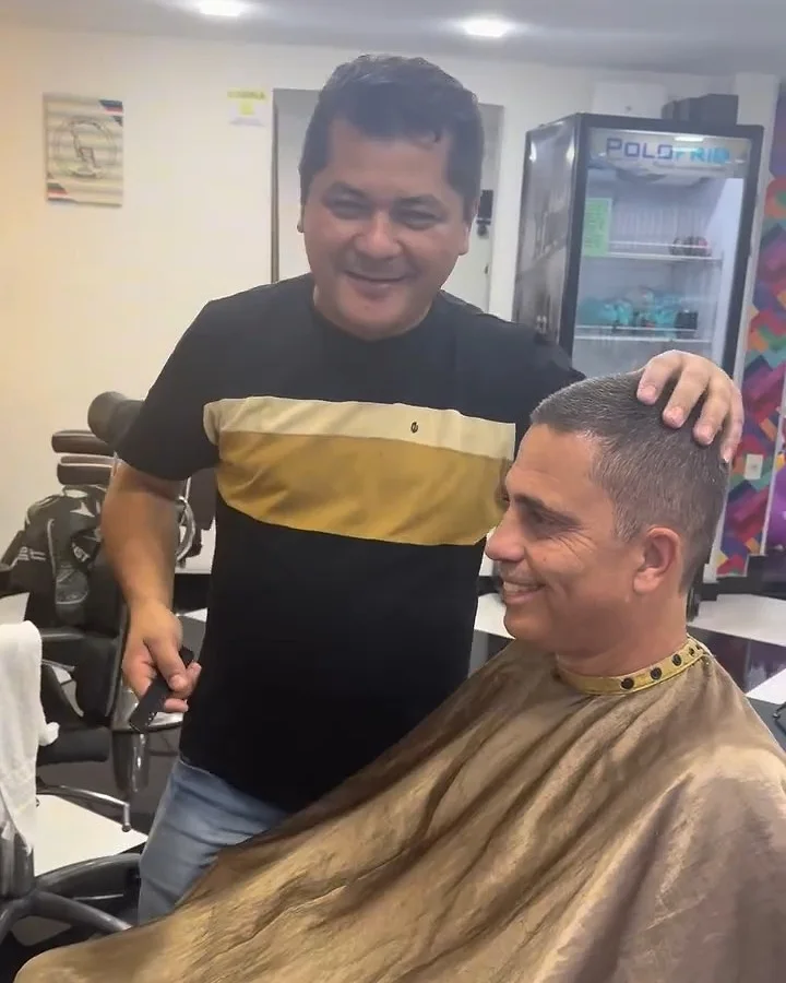 Barbeiro rindo com um cliente adulto na cadeira da Barber VIPs
