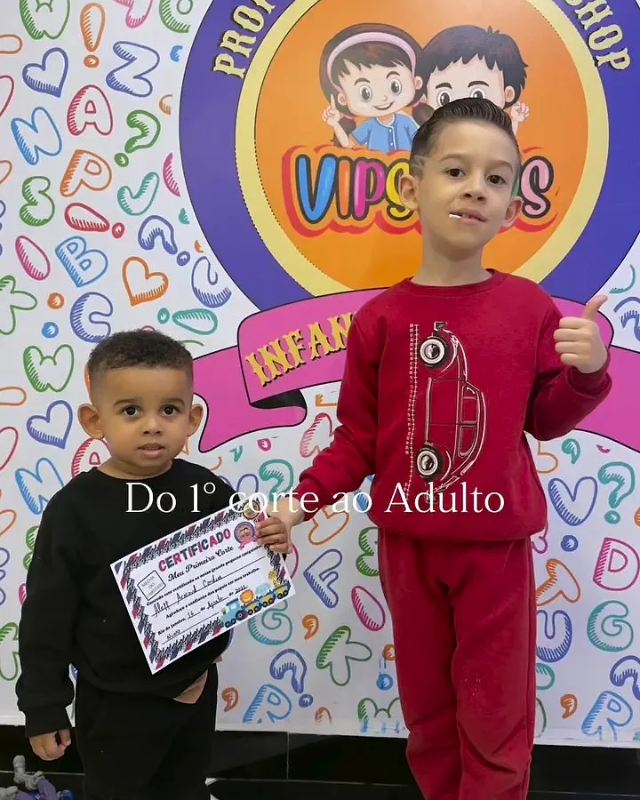 Dois irmãos com certificado em frente ao painel colorido VIPs Kids