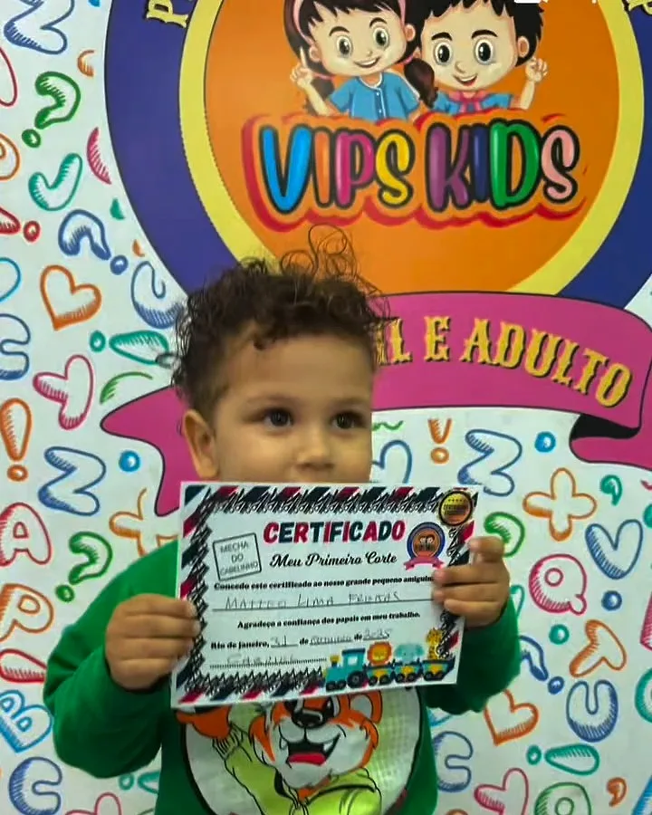 Menino com o certificado do primeiro corte em frente ao painel da VIPs Kids