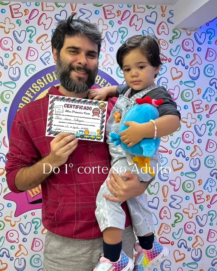 Pai com a criança no colo segurando o certificado do primeiro corte
